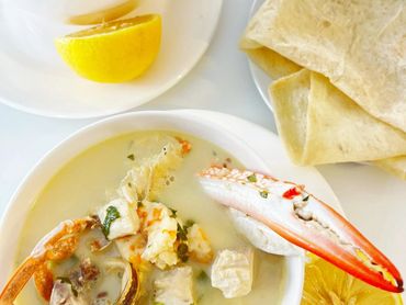 Two bowls of creamy seafood soup with lemon and flatbread on the side.