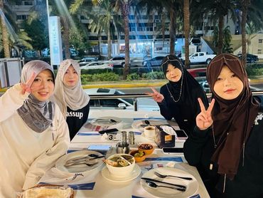 Four women in hijabs enjoying a meal at Fares Restaurant, posing with peace signs.