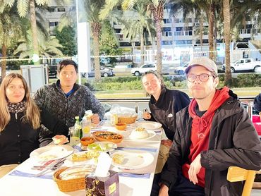 Four friends enjoying a nighttime outdoor dinner under palm trees.