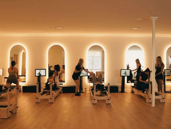People exercising on reformer machines in a modern Pilates studio.