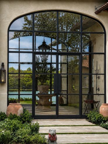 Elegant arched glass door with black metal frame reflecting outdoor greenery and a lake.