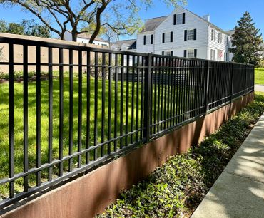 Black metal fence along a landscaped garden with a white house in the background.