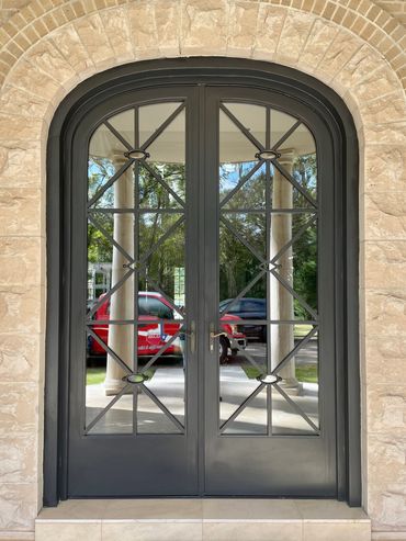 Elegant black iron double door with glass panels framed by stone and brick.