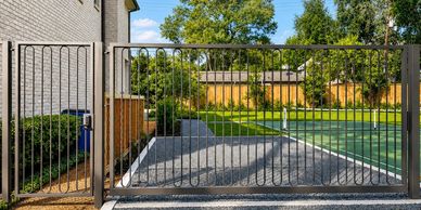A modern black metal gate enclosing a backyard with a tennis court.