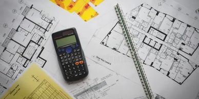 Architectural plans with calculator and scale ruler on table.