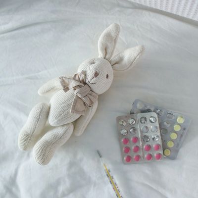 Syringe and 2 packets of tablets next to a white bunny doll on a white hospital bed.