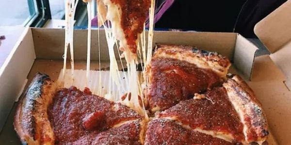 A cheesy deep-dish pizza slice being lifted with stretchy melted cheese.