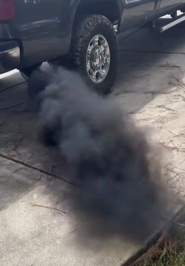Thick black smoke emitting from a truck's exhaust on a driveway.