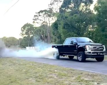 A black pickup truck performing a burnout on a road, emitting thick smoke.