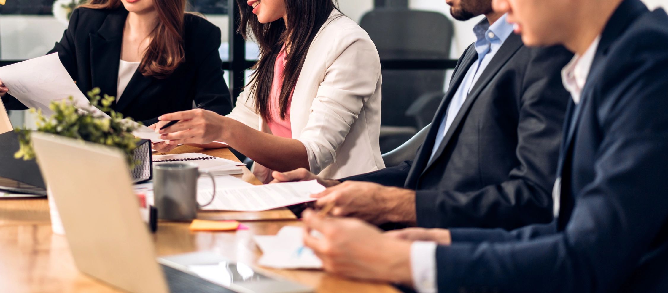 Four professionals collaborate, reviewing documents at a conference table in a modern office setting.