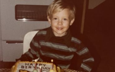 A young boy smiling with a birthday cake in front of him.
