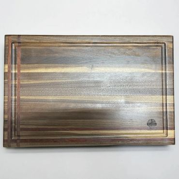 Rectangular wooden cutting board with multiple wood tones and a groove around the edge.