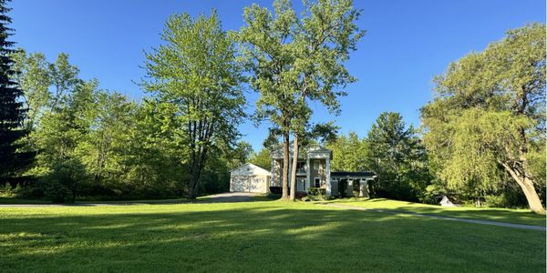 A large green lawn with trees and a house under a clear blue sky.