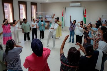 A lively group participating in an interactive workshop in a bright room with Jordanian flags.