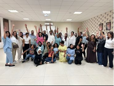 A diverse group of people smiling and waving indoors.