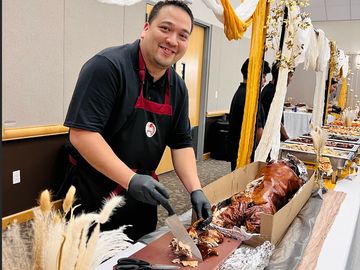 Man slicing roasted pig at a festive buffet table.