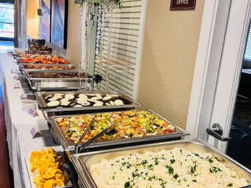 A buffet table with trays of rice, salad, grilled vegetables, and orange slices.