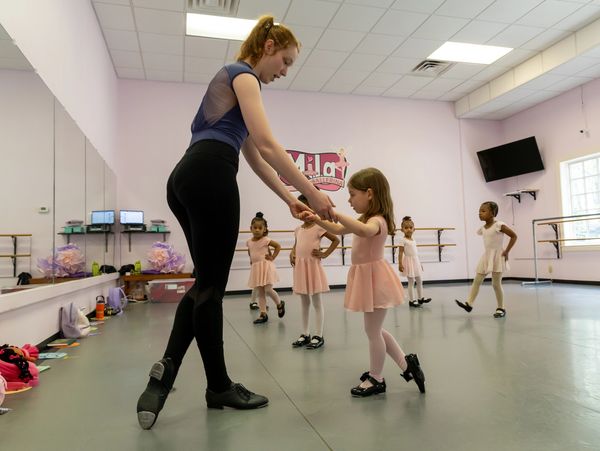 Dance teacher guiding a young girl in tap dance class.