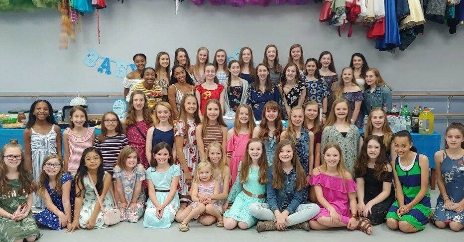 Large group of girls posing together in colorful dresses indoors.