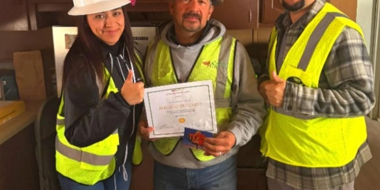 Three workers in safety gear, one holding a certificate, posing under 'SAFETY 1ST' sign at Aztec Ready Mix El Paso TX.