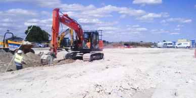 Construction site featuring a red digger and worker wearing reflective gear and helmet
