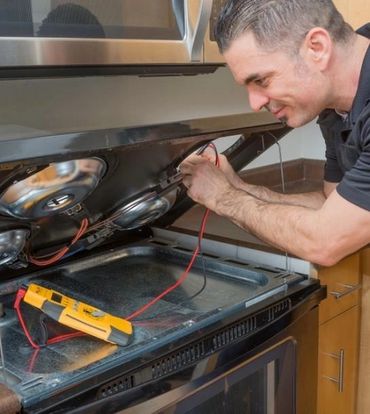 Technician repairing the oven's internal wiring with a multimeter.