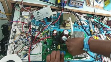 Hands working on an electronic circuit board with wires and components.