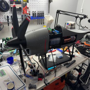 A detailed model airplane engine setup on a cluttered workbench with tools and wiring.