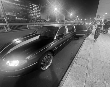 Night scene with a luxury black limousine parked by the sidewalk near a hotel.