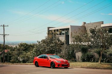 Red sports car parked on a suburban street in front of modern houses.