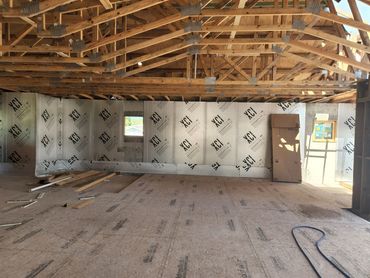 Interior of a building under construction with exposed roof trusses and insulation panels.