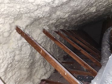 Spray foam insulation applied between attic wooden beams.
