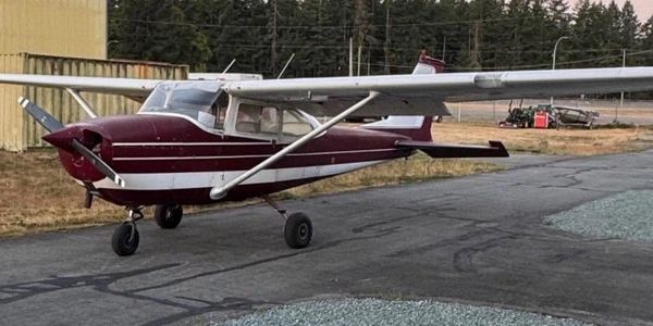 A small maroon and white single-engine airplane parked on a tarmac near a hangar.