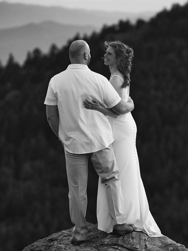 Bride and groom embracing on a rocky outcrop with mountain views during their black and white Roan M
