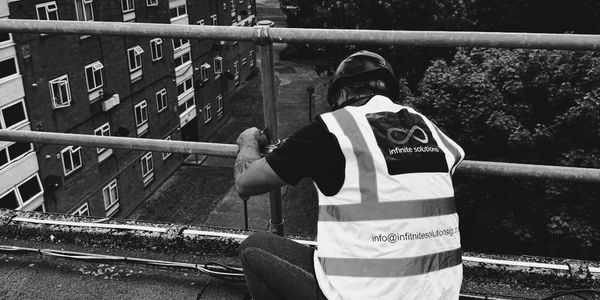 Construction worker in safety vest and helmet working on rooftop railing.