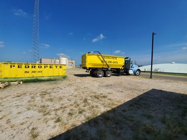 Yellow Pedro Pete dumpsters and truck in an industrial area under a clear blue sky.