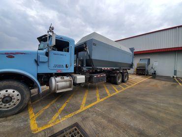 Blue Peterbilt dump truck parked near a loading dock on a cloudy day.