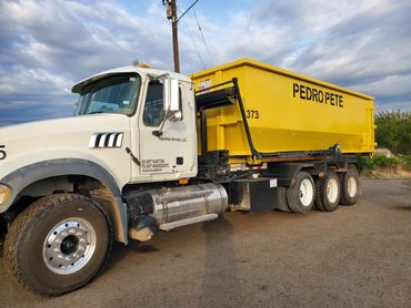 White truck with a bright yellow container labeled PEDRO PETE parked on a dirt road.