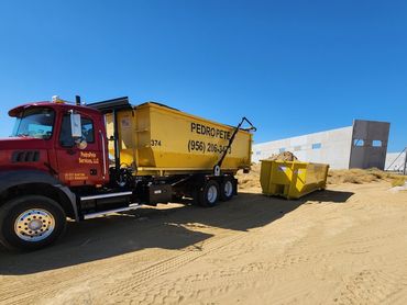 Construction truck and dumpsters on a sandy site under clear blue sky.