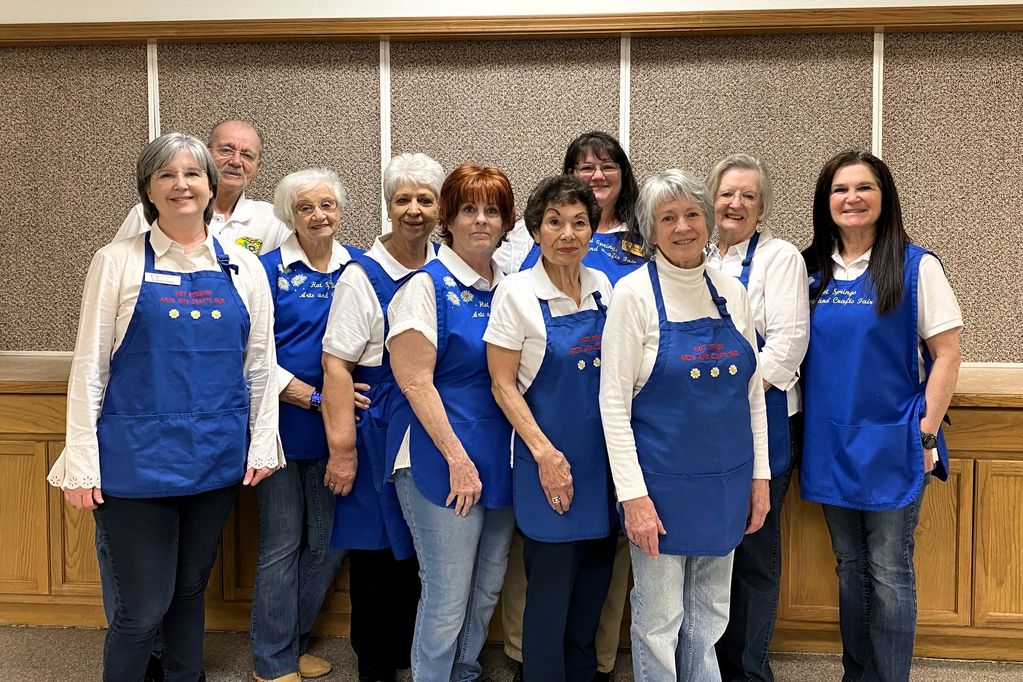 Group of smiling women and one man wearing white shirts and blue aprons 