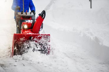 Person using a red snowblower to clear heavy snow on a path.