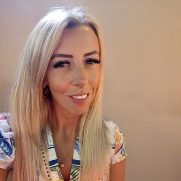Smiling woman with long blonde hair in colorful patterned blouse.