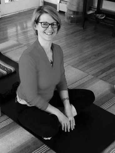a black and white photo of Heather Horton, LMT sitting on a yoga mat and smiling