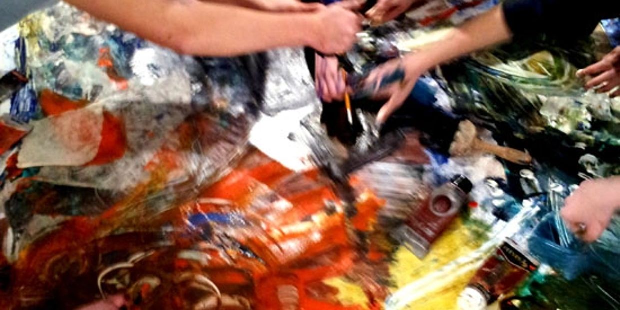 Multiple hands engaged in a vibrant, abstract painting session with colorful paints and brushes.