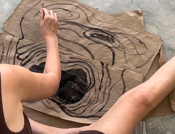 Person drawing abstract black shapes on a large brown paper sheet.