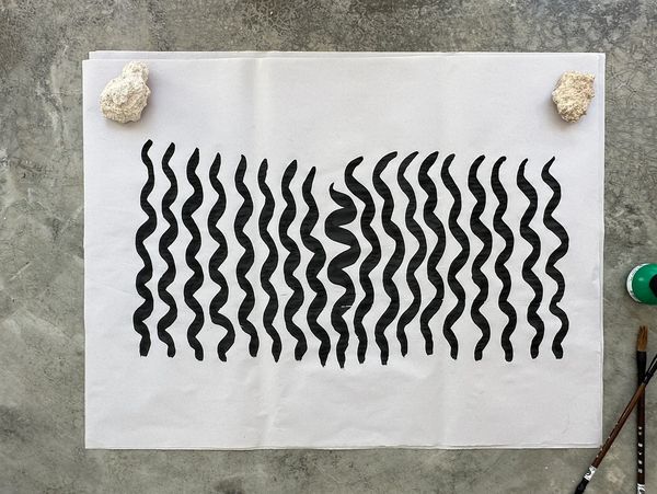 Black wavy lines printed on white paper, held by rocks.