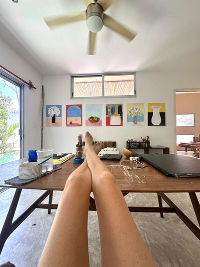 Person relaxing with legs on a wooden table in a bright, art-filled room.