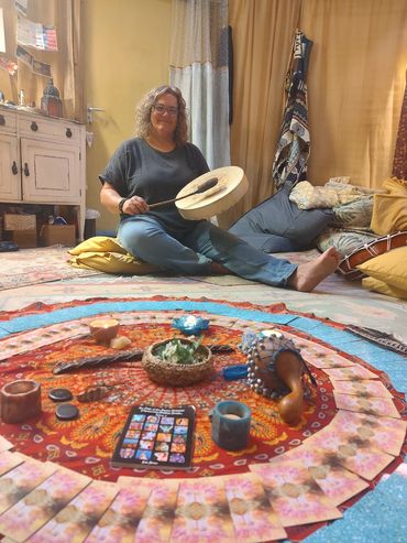 Anna sitting with her drum with a red alter cloth set out with saining stick and feathers, rattles,