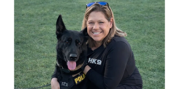 Woman smiling with her police dog outdoors.