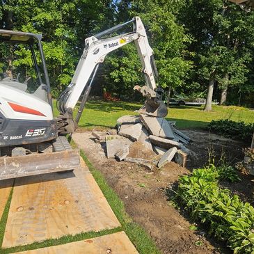 A Bobcat excavator breaking concrete in a garden area.